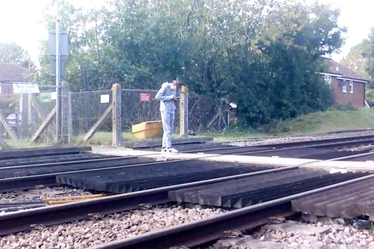 A pedestrian looking at a mobile phone on the tracks. Shocking CCTV footage captures the danger of pedestrian distractions at level crossings.  Release date - April 29, 2025.  The montage footage highlights the potential risks of losing focus near a railway line, from a teenager stood in the middle of a level crossing gazing at their mobile phone, to a pram-pushing couple failing to observe safety barrier alarms.  In a world full of distractions, Network Rail is warning of the more serious consequences of being distracted at level crossings. Over the past four years**, there have been 1,574 recorded near miss incidents involving pedestrians at level crossings.  Over that same period, incidents have increased on average by 16% from April to May.